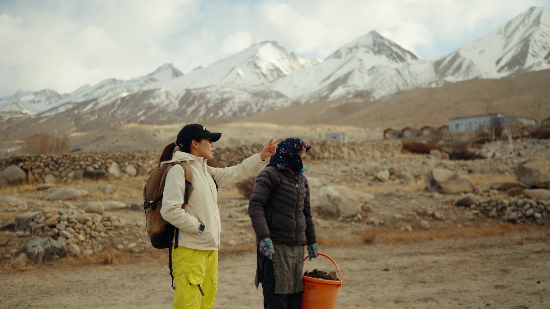 Stanzin pointing toward snow-capped peaks with a local villager beside her