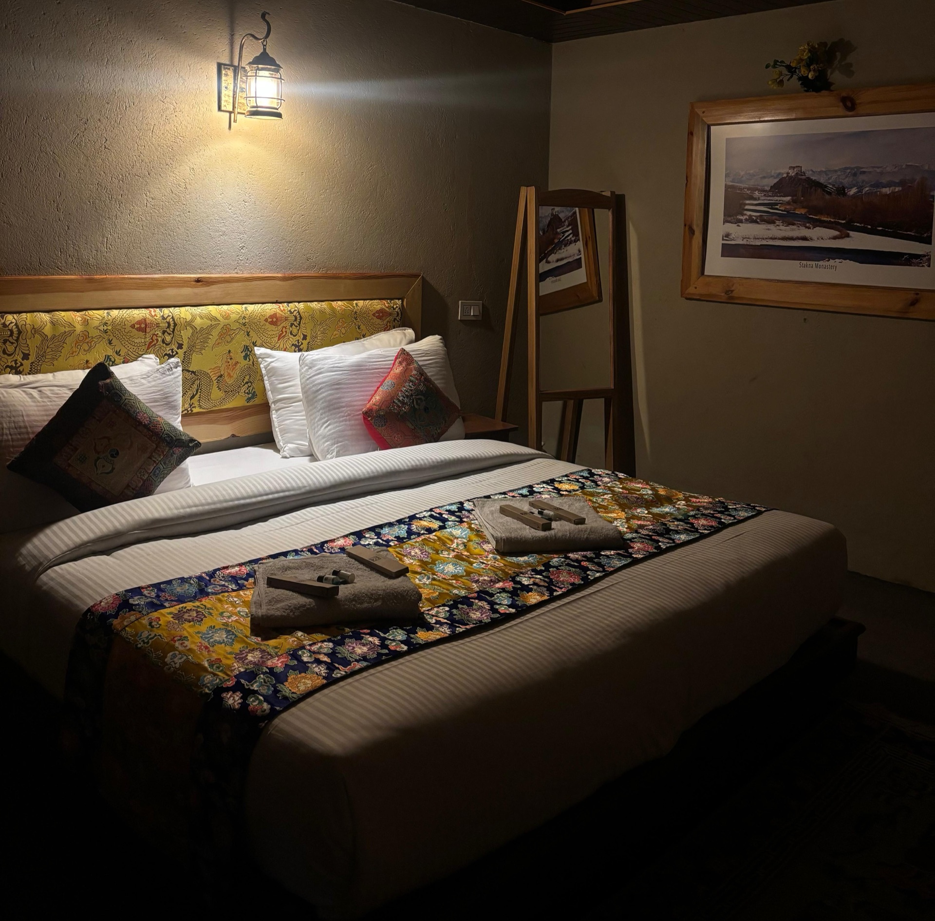 Warmly lit hotel room with Ladakhi textile bed runner, wall lamp and framed monastery print