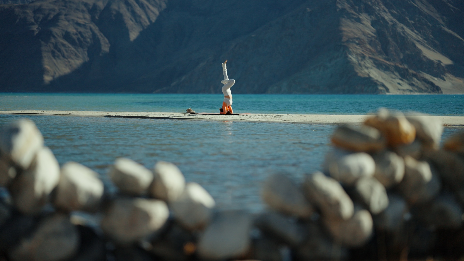 Yoga headstand at Pangong Tso with stone cairns in foreground