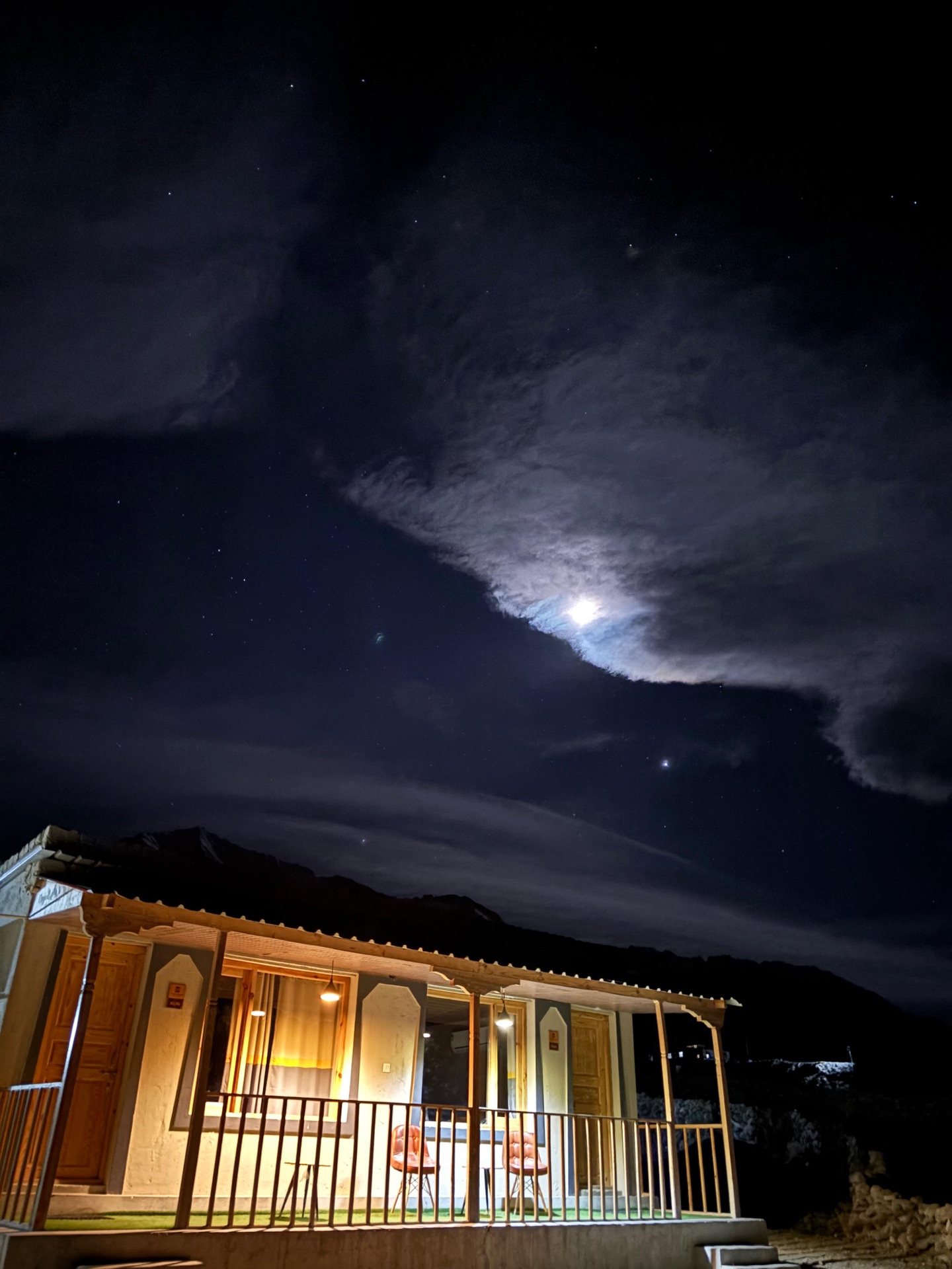 Guesthouse lit at night with a moonlit star-filled sky above the mountains