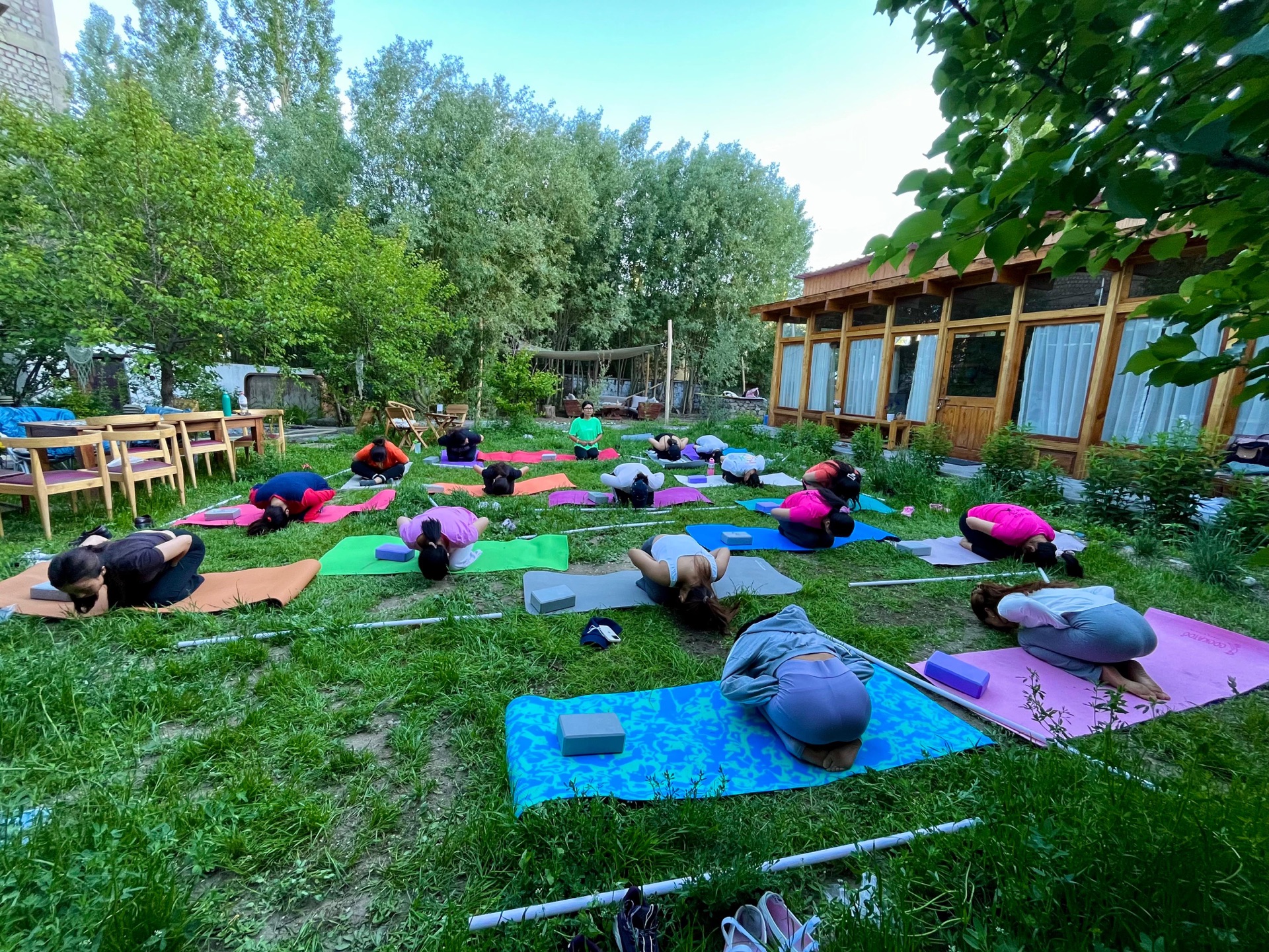 Stanzin leading a group yoga session on grass in a lush garden setting